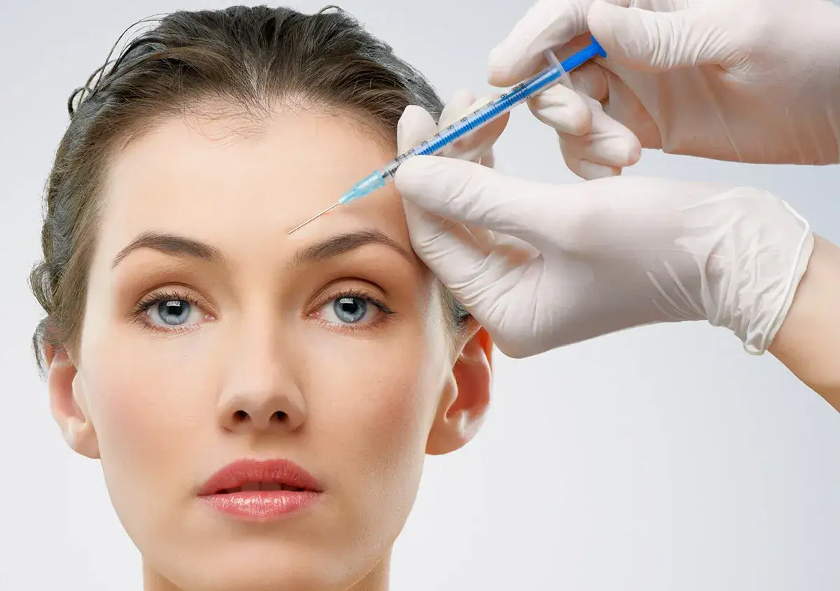 Eine Hand in einem weißen Handschuh injiziert Botox in die Stirn einer Frau für ein glatteres Aussehen.