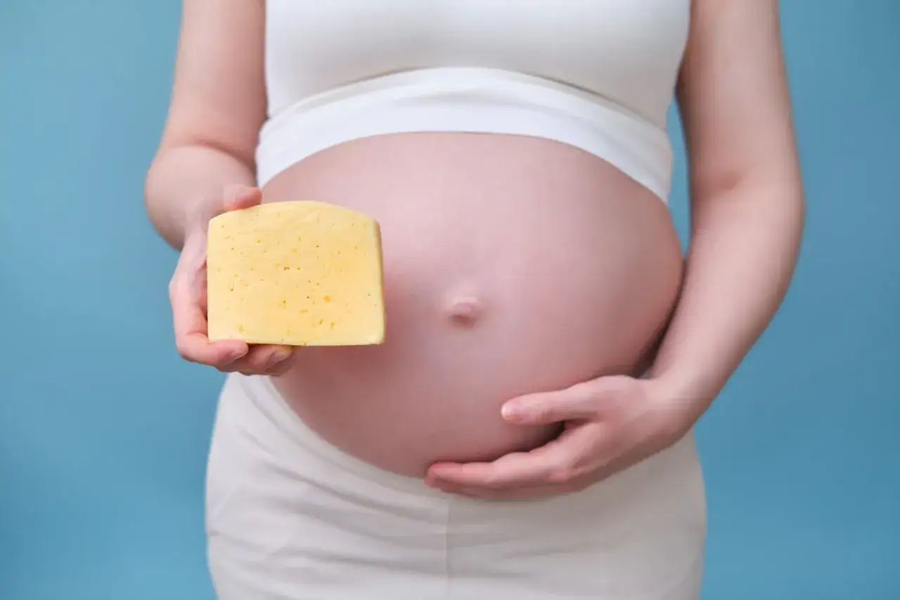Schwangere hält ein Stück Mozzarella vor ihrem Bauch.