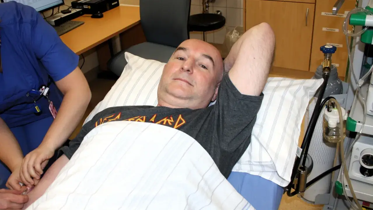 Mann liegt im Bett, bereit f&uuml;r eine Darmspiegelung. Eine Krankenschwester legt eine Infusion. Warum nicht duschen vor Darmspiegelung?