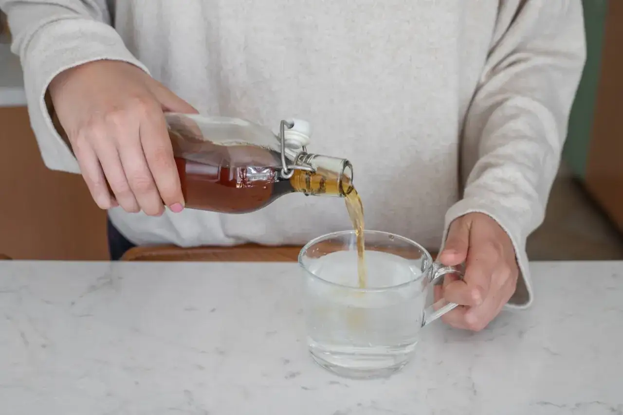 Eine Person gießt Apfelessig in ein Glas Wasser. Ein gesunder Start in den Tag für das Abnehmen.