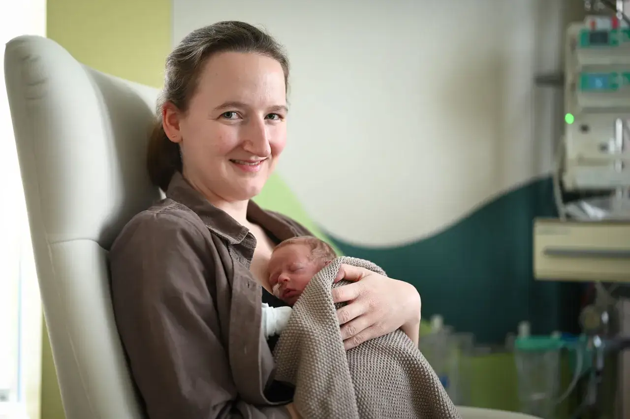 Glückliche Mutter hält ihr Neugeborenes im Arm. Die Frage, wie lange nach Geburt im Krankenhaus, ist hier nicht relevant, da die Szene Geborgenheit zeigt.